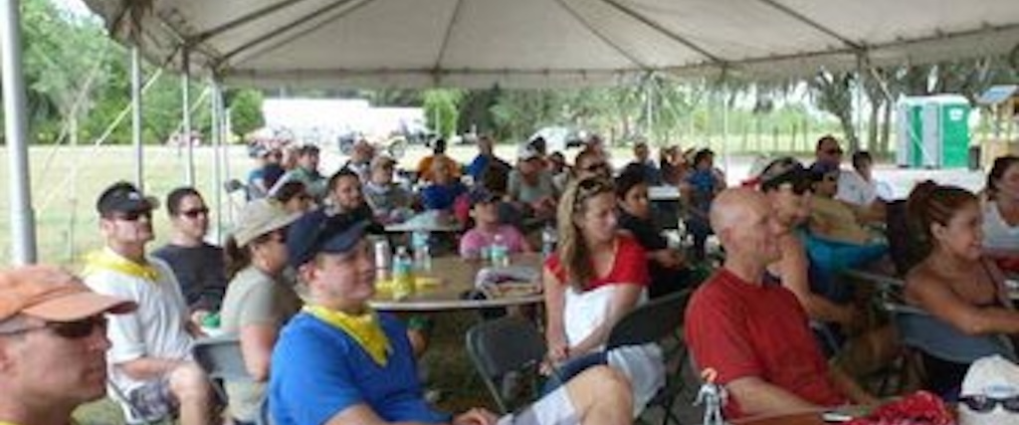 Large group of people sitting under a tent at an outdoor event.